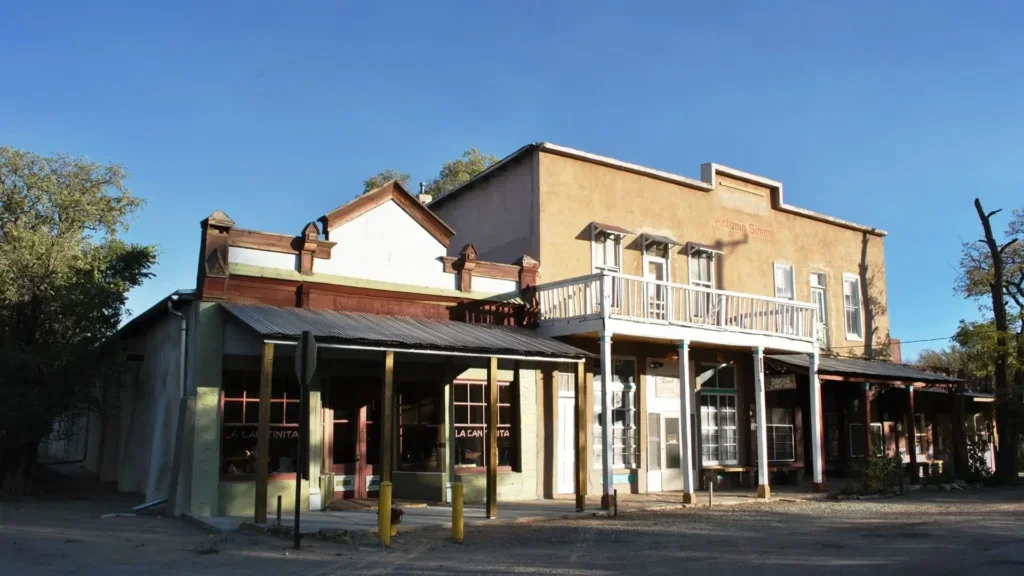 A small street view of a historic building with a balcony, storefronts, and a street in front under a clear blue sky.