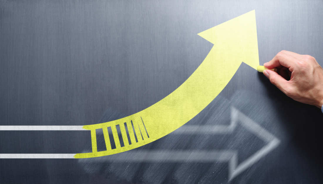 A person's hand drawing a yellow upward arrow with chalk on a blackboard, illustrating growth or progress.