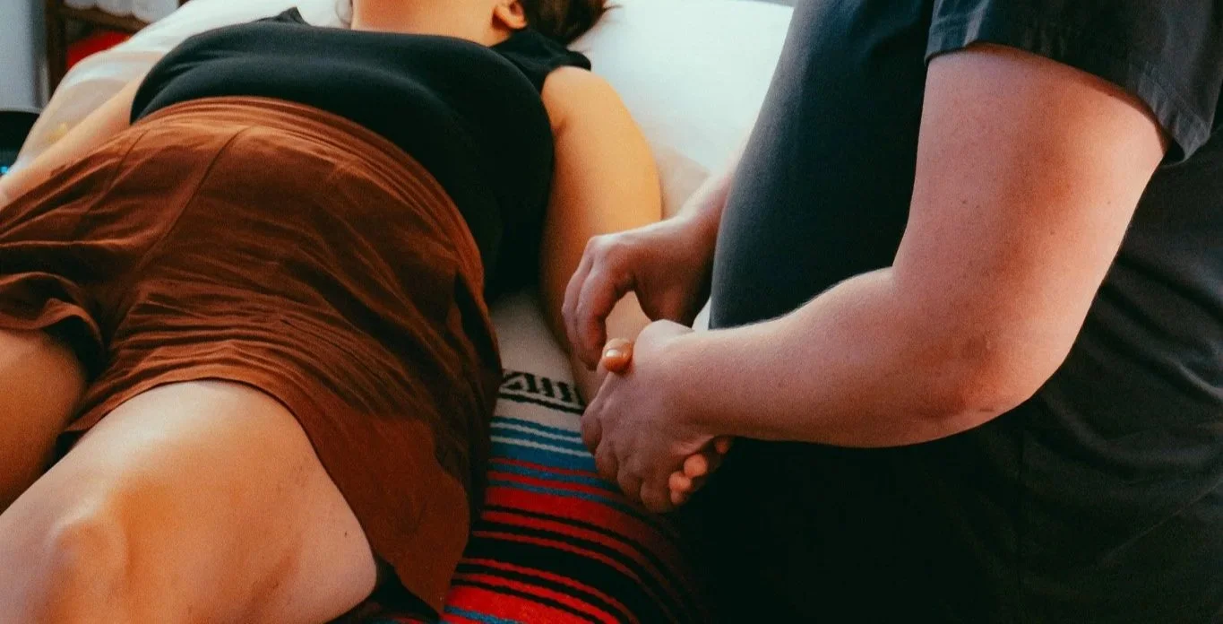 Melissa stands next to a patient while taking their pulse. She gently holds the patient's hand while taking the pulse.