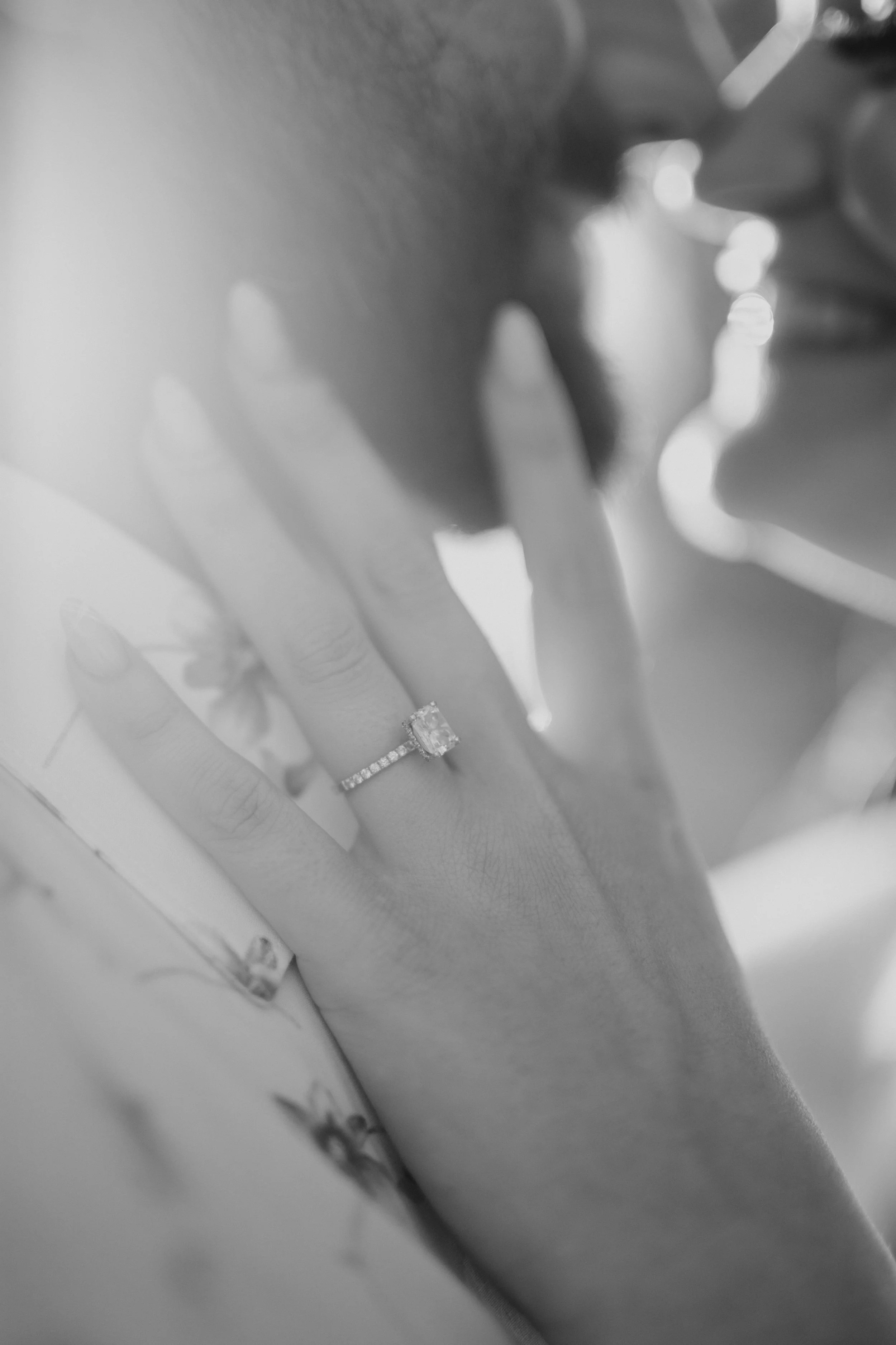 Close-up of a hand with a large gemstone ring on the ring finger, with sunlight creating highlights and shadows, in black and white.