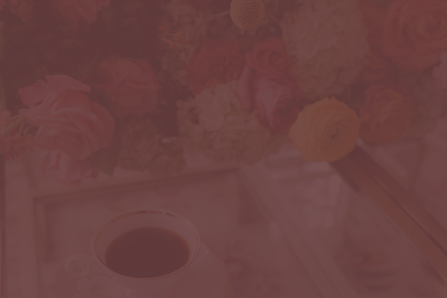 A floral arrangement with pink, orange, and yellow roses, and a cup of coffee on a table.