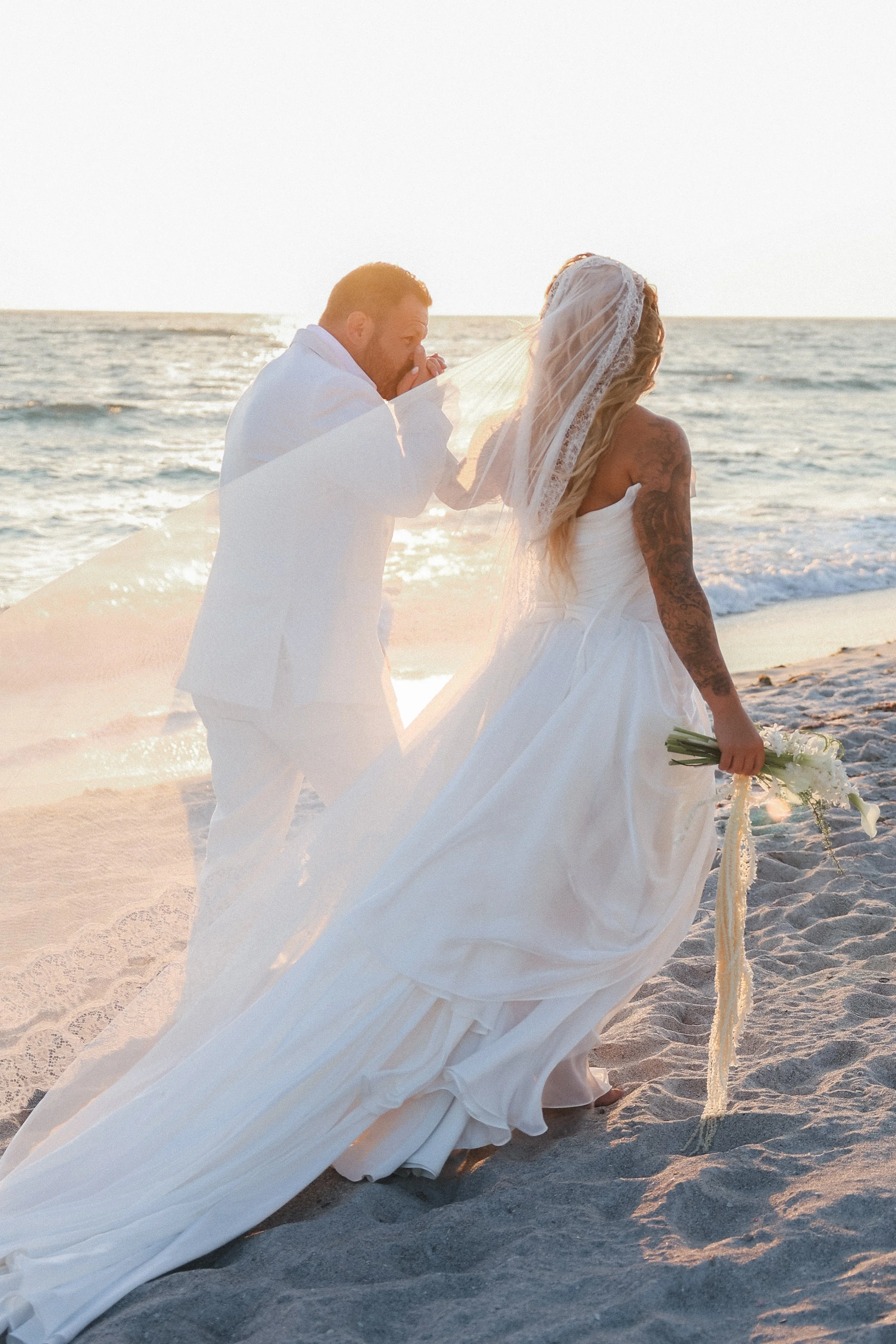 Groom kissing bride's hand on the beach at sunset at the St. Regis Longboat Key, Tampa Bay luxury wedding photographer Divine Design Photography