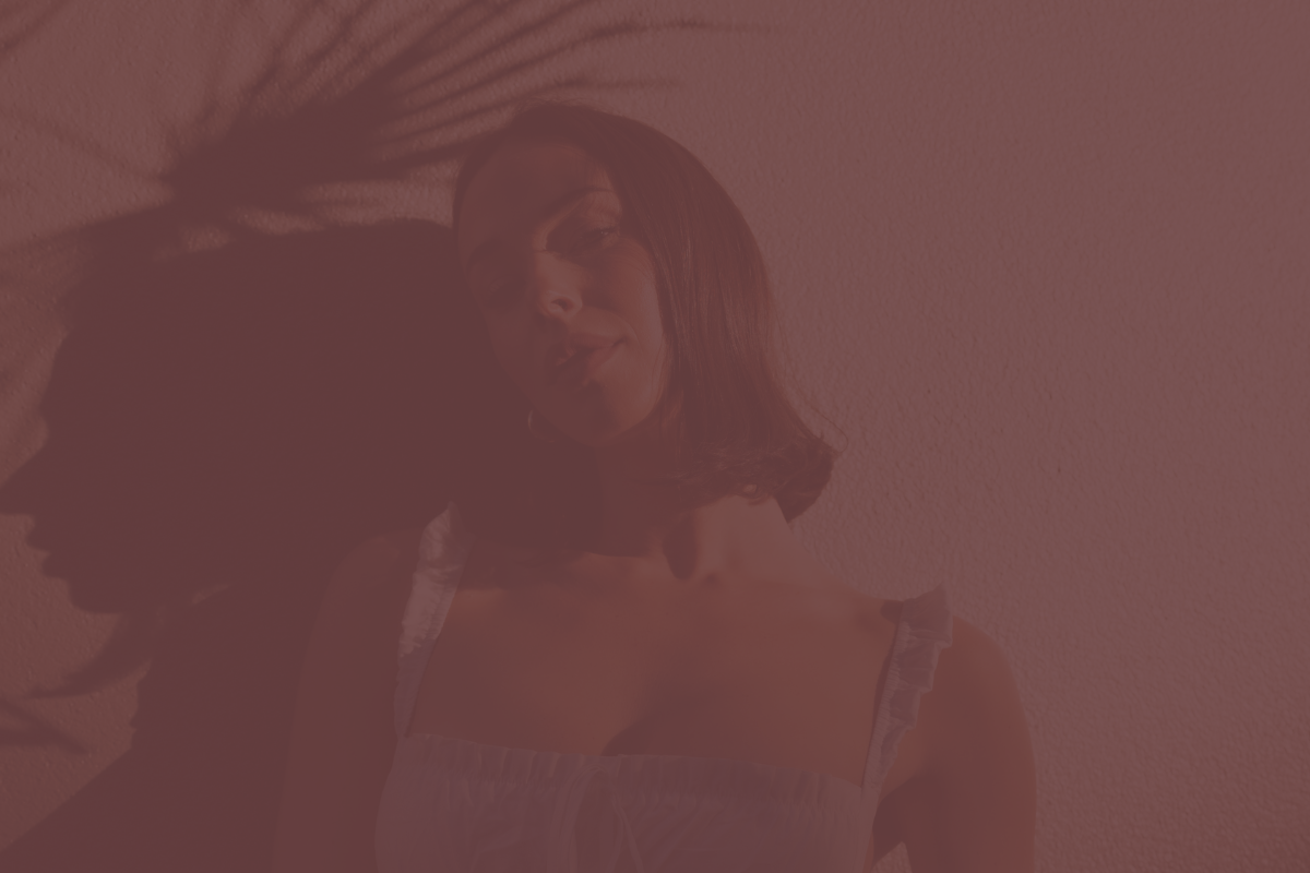 A woman with shoulder-length dark hair smiling and posing against a textured pink wall.