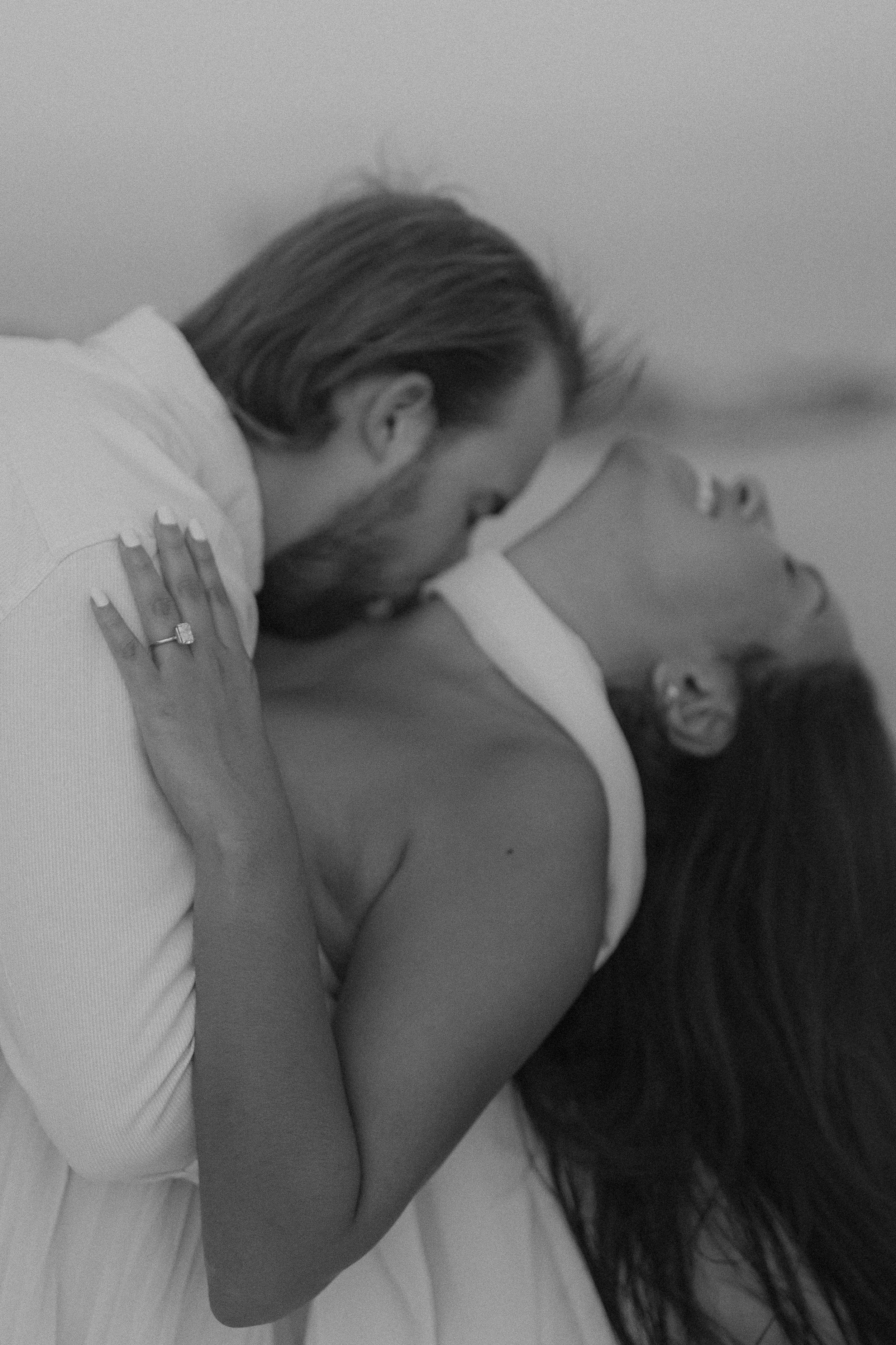 A person with long hair leaning over another person lying on a bed, appearing to kiss or whisper closely.