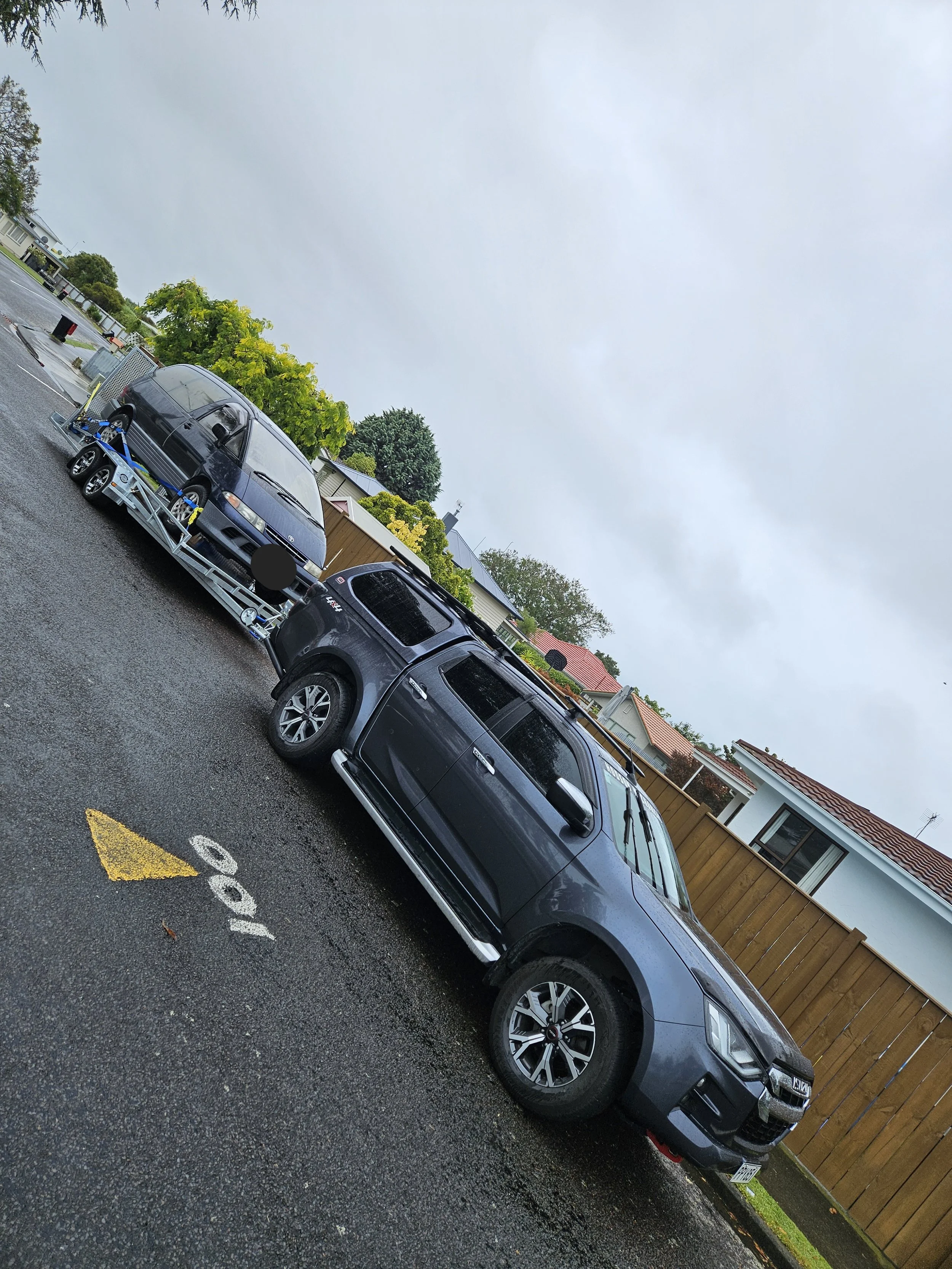 A grey SUV parked in a wet parking spot next to a trailer carrying a blue car. The parking spot is marked with the number 160.