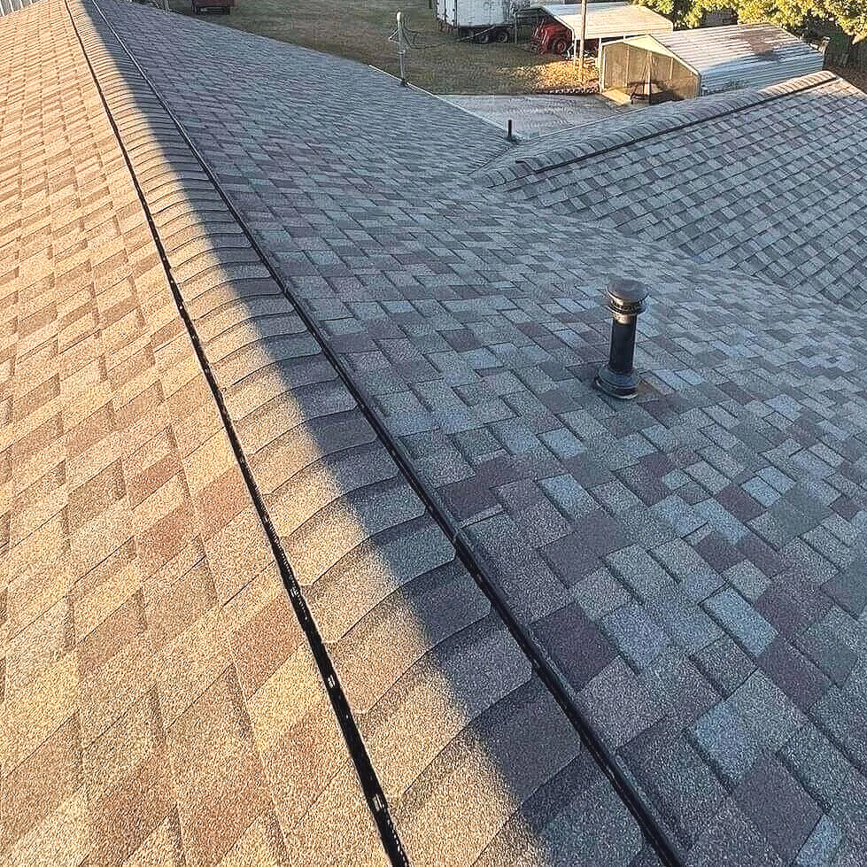 A house roof covered with gray asphalt shingles, with a vent pipe and a ridge vent visible.