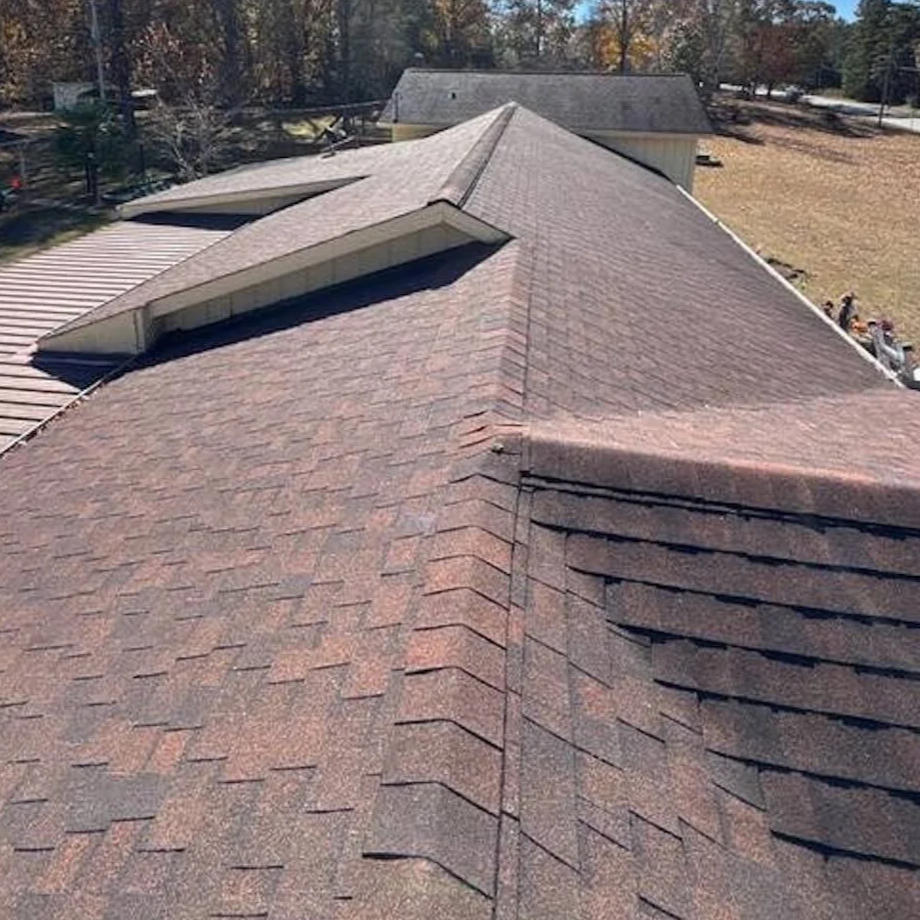 A rooftop with several ridges and shingles, showing an intersection of roof sections in a residential area.