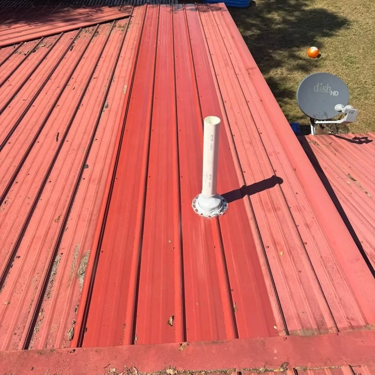 Red metal roof with a white PVC pipe protruding, a satellite dish labeled 'dish HD,' and an orange ball on the grass nearby.