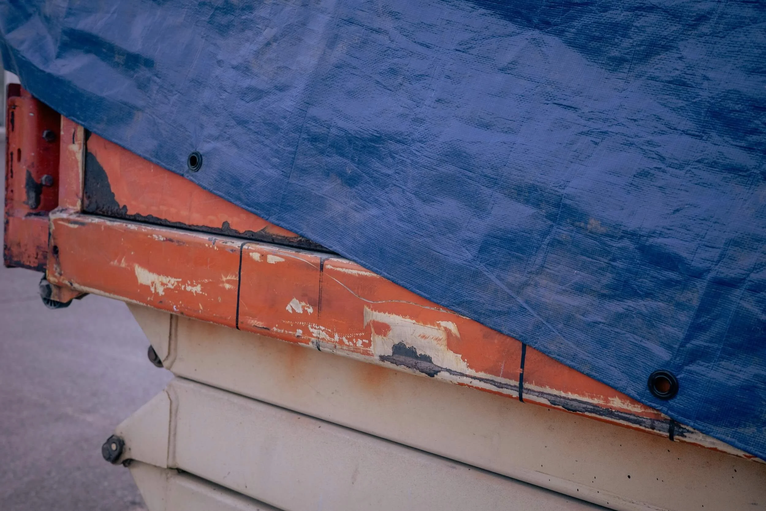 Close-up of stacked industrial containers with worn paint, rust, and a blue tarpaulin covering the top container.