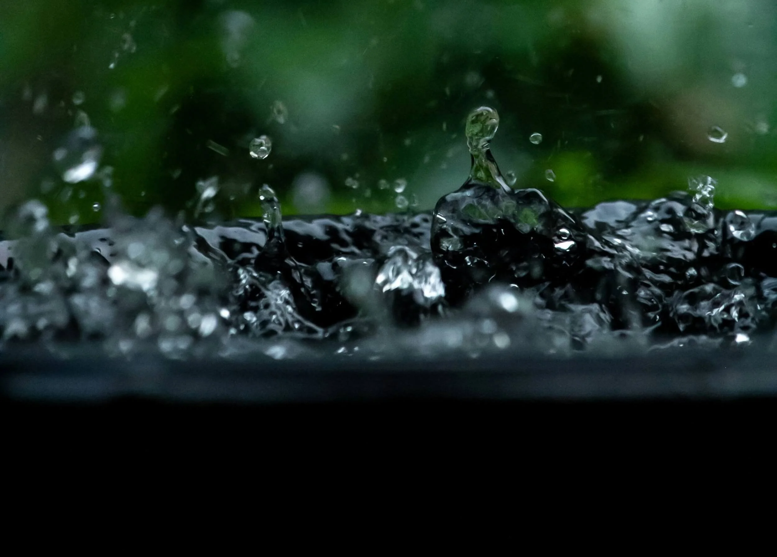 Close-up of water splashing on a dark surface with a blurred green background.