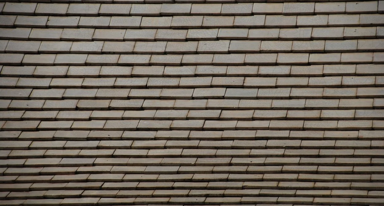 A close-up view of a roof with overlapping beige shingles.
