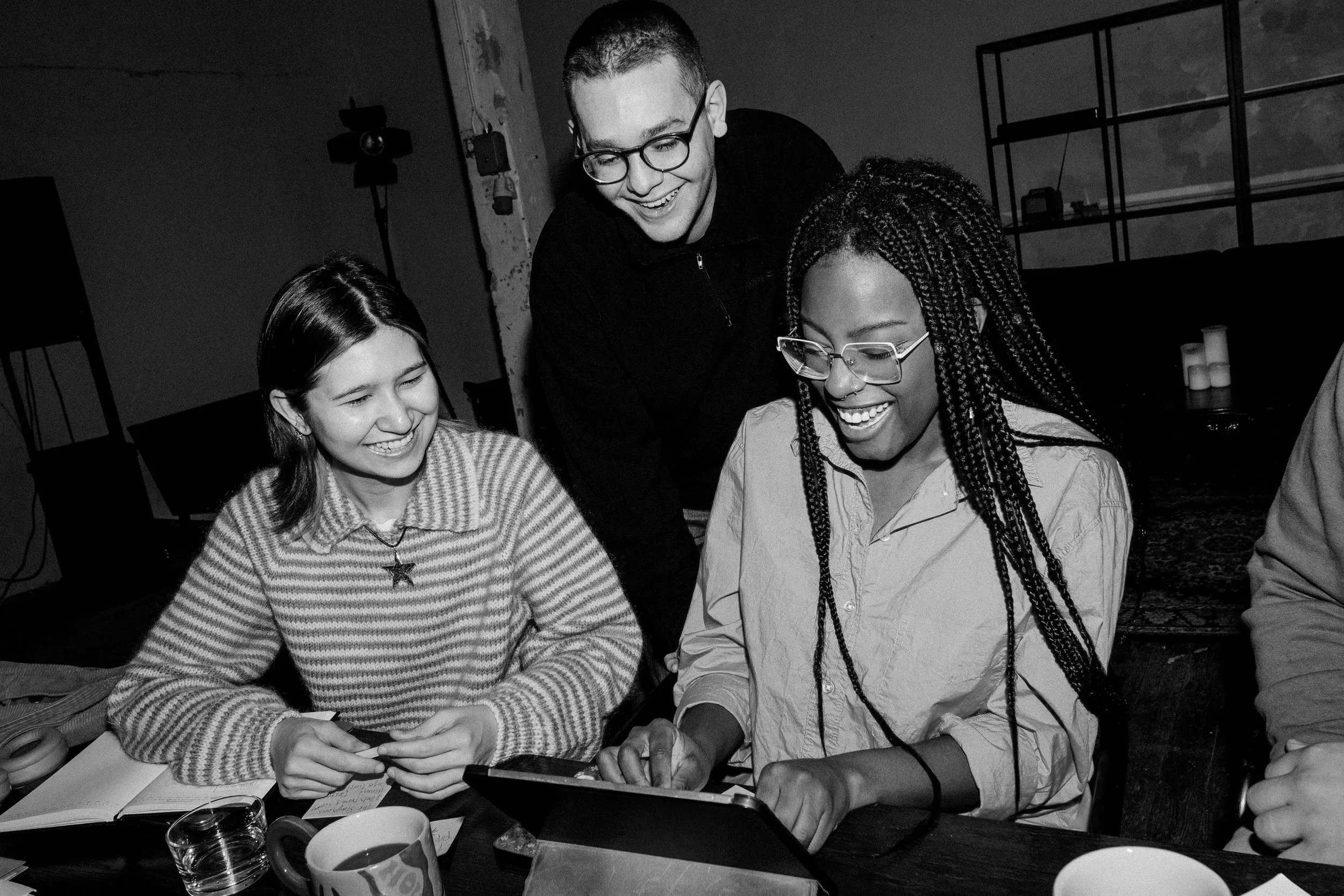 Groupe de jeunes gens rieurs, assis autour d'une table, regardant un téléphone, dans une ambiance conviviale.
