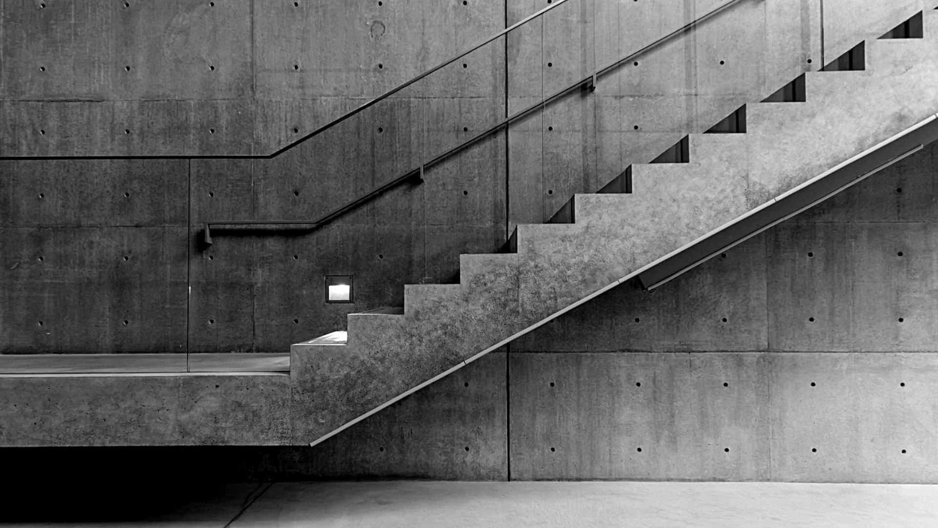 An interior shot of a concrete staircase with metal handrails against a concrete wall.