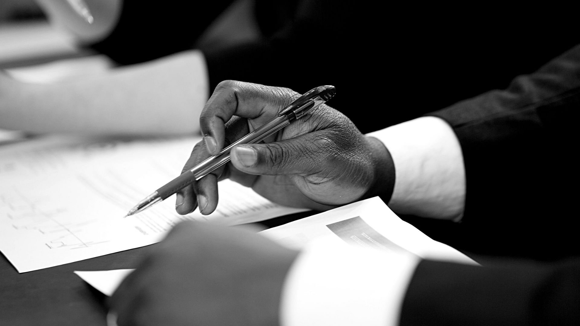 Close-up of a person's hand holding a pen and writing on papers placed on a table.