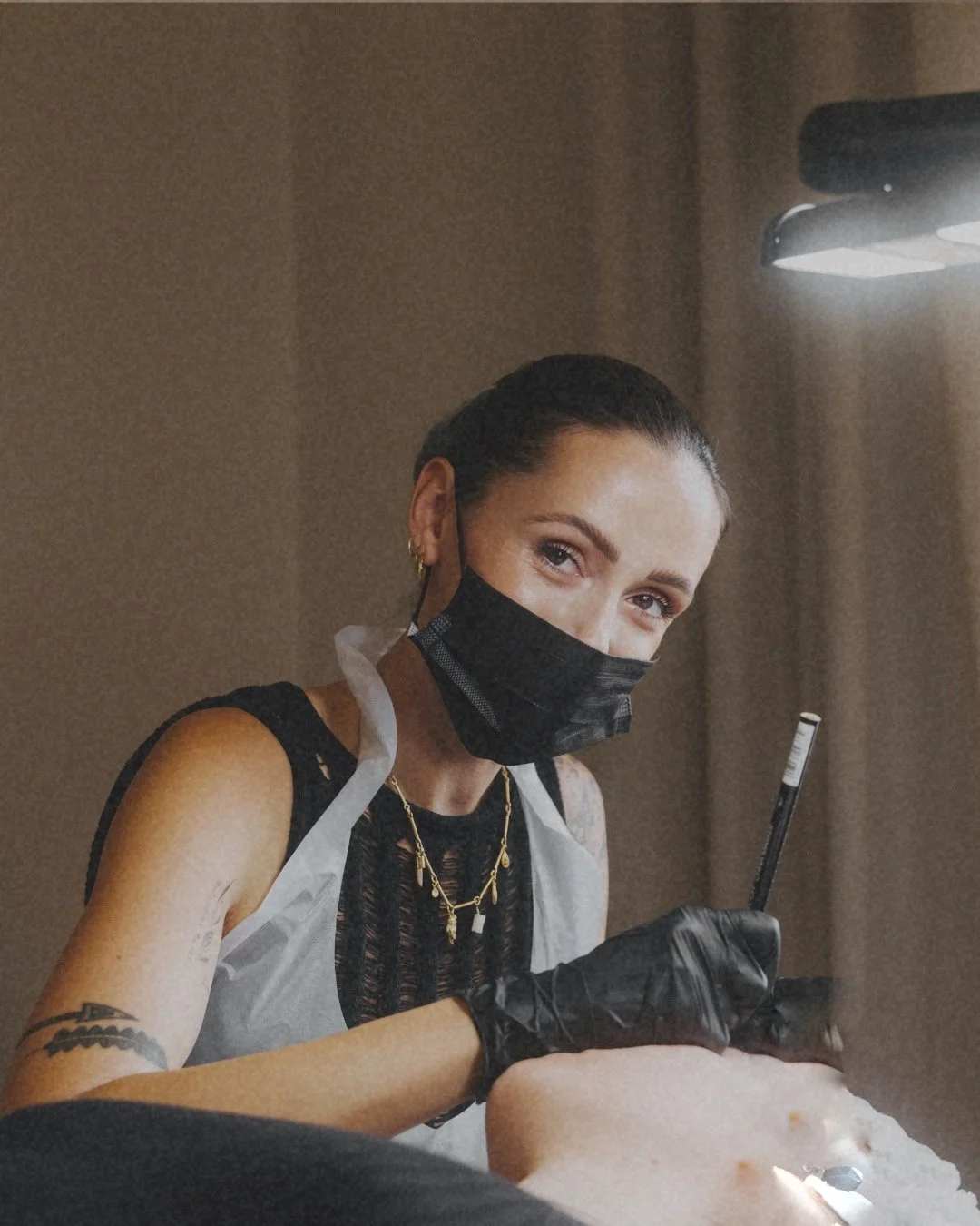 Tattooed woman mit schwarzen Haaren, schwarzer Maske, schwarze Handschuhe und goldene Ketten tätowiert, die Tätowierung macht.