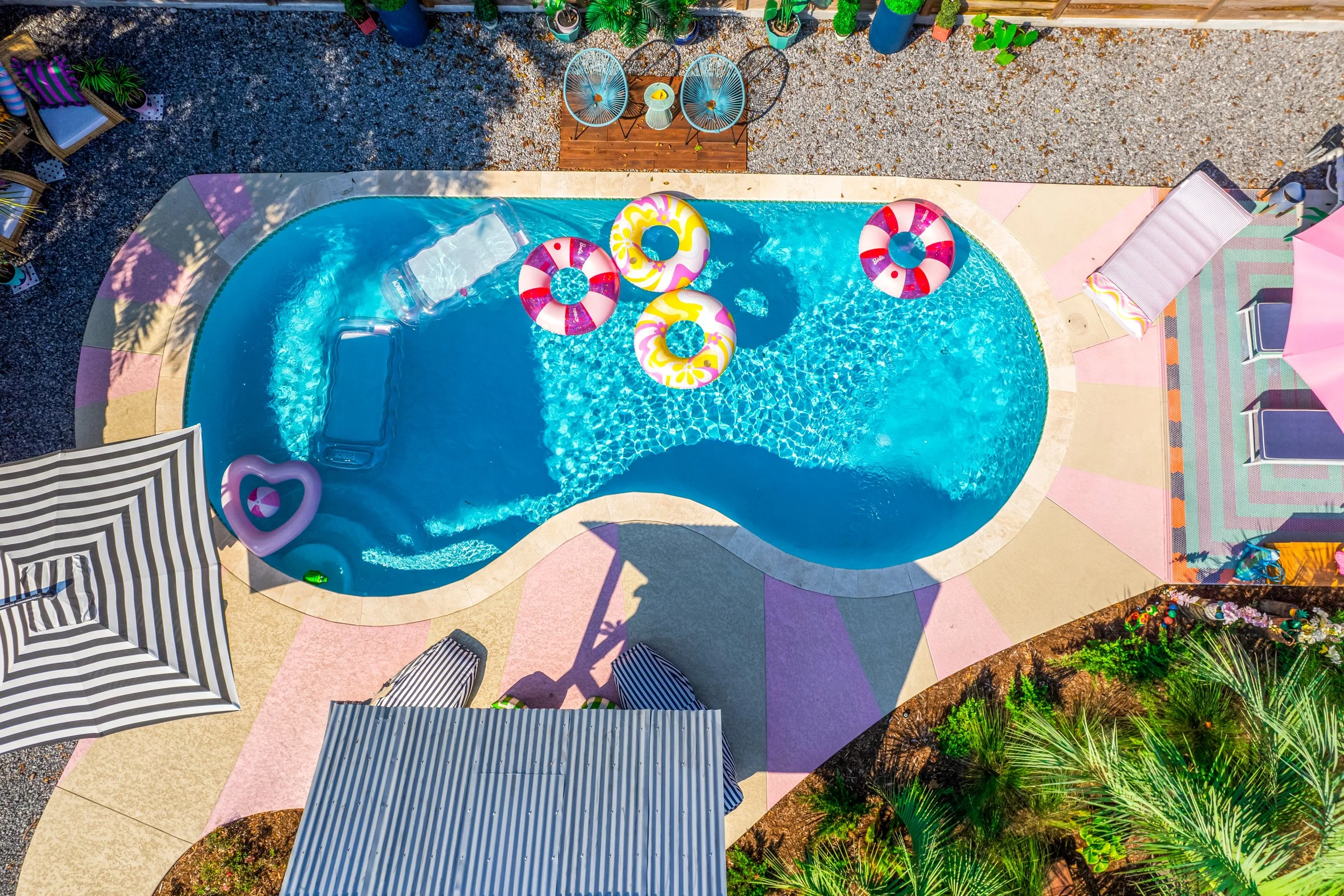 Luxury Listing pictures with Aimee (Amay) Curole, Top Realtor in Metairie, 23 Realty.  An aerial view of a backyard swimming pool with floaties, surrounded by outdoor furniture, umbrellas, and plants.