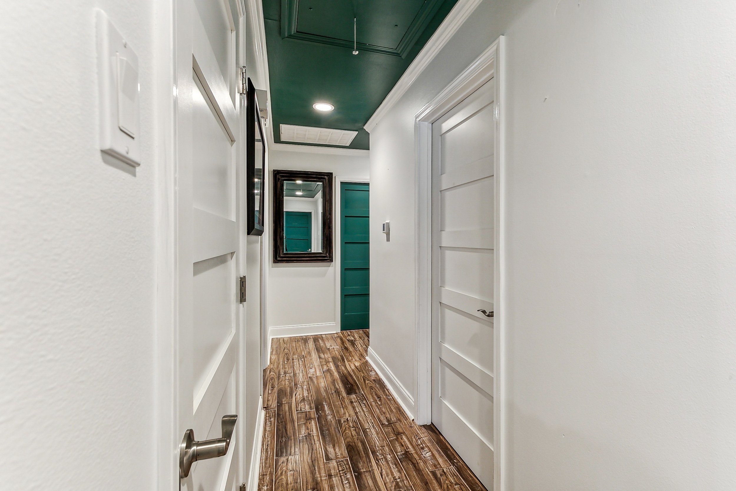 Rockwood Green painted ceiling adds the illusion of higher ceilings in the hallway with Aimee (Amay) Curole, Top Realtor in Metairie, 23 Realty. Hallway with white walls, wooden floor, and doors.