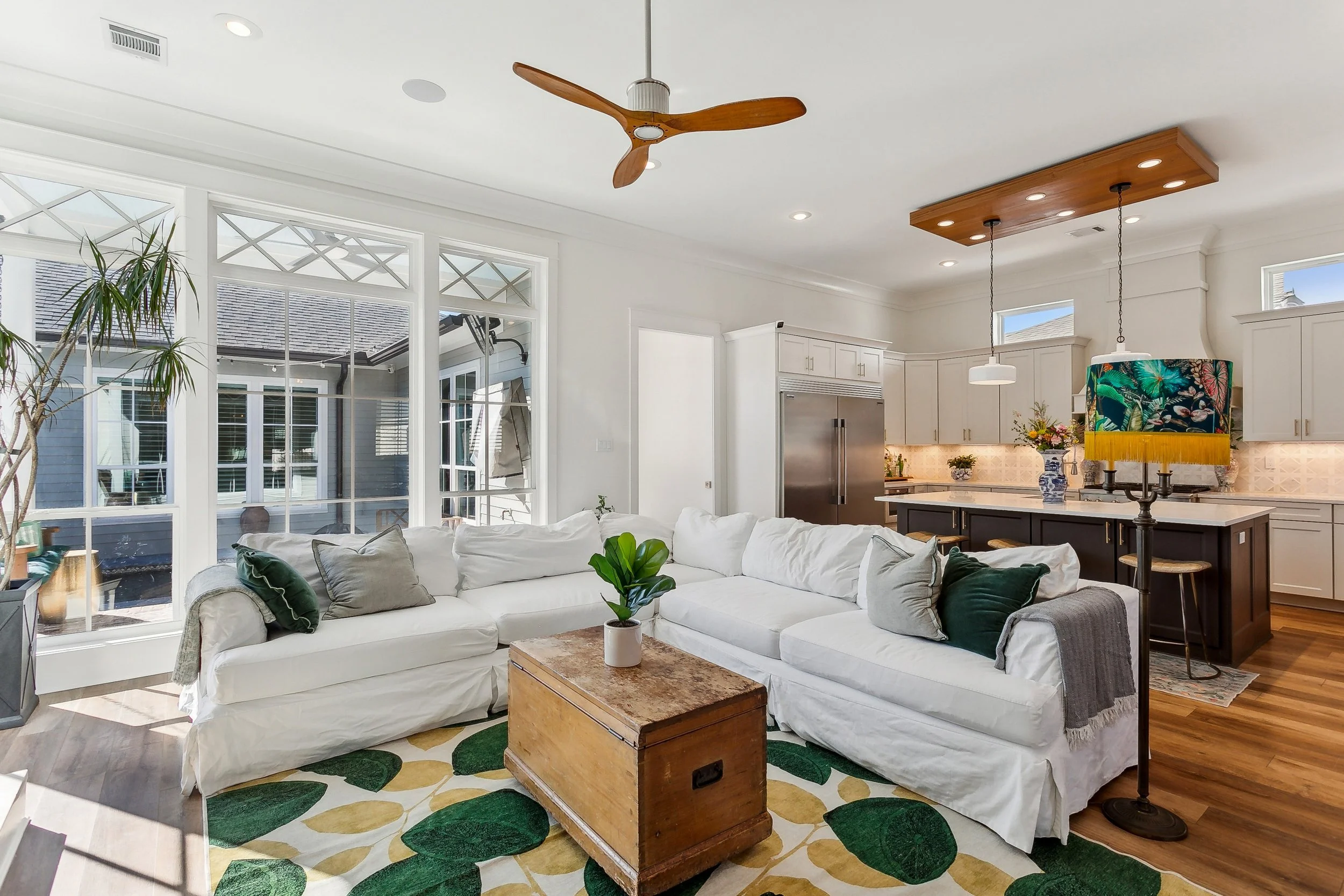 Luxury Listing pictures with Aimee (Amay) Curole, Top Realtor in Metairie, 23 Realty.   Bright living room with a white sectional sofa, green and gray pillows, wooden coffee table, area rug with leaf pattern, large windows, open kitchen