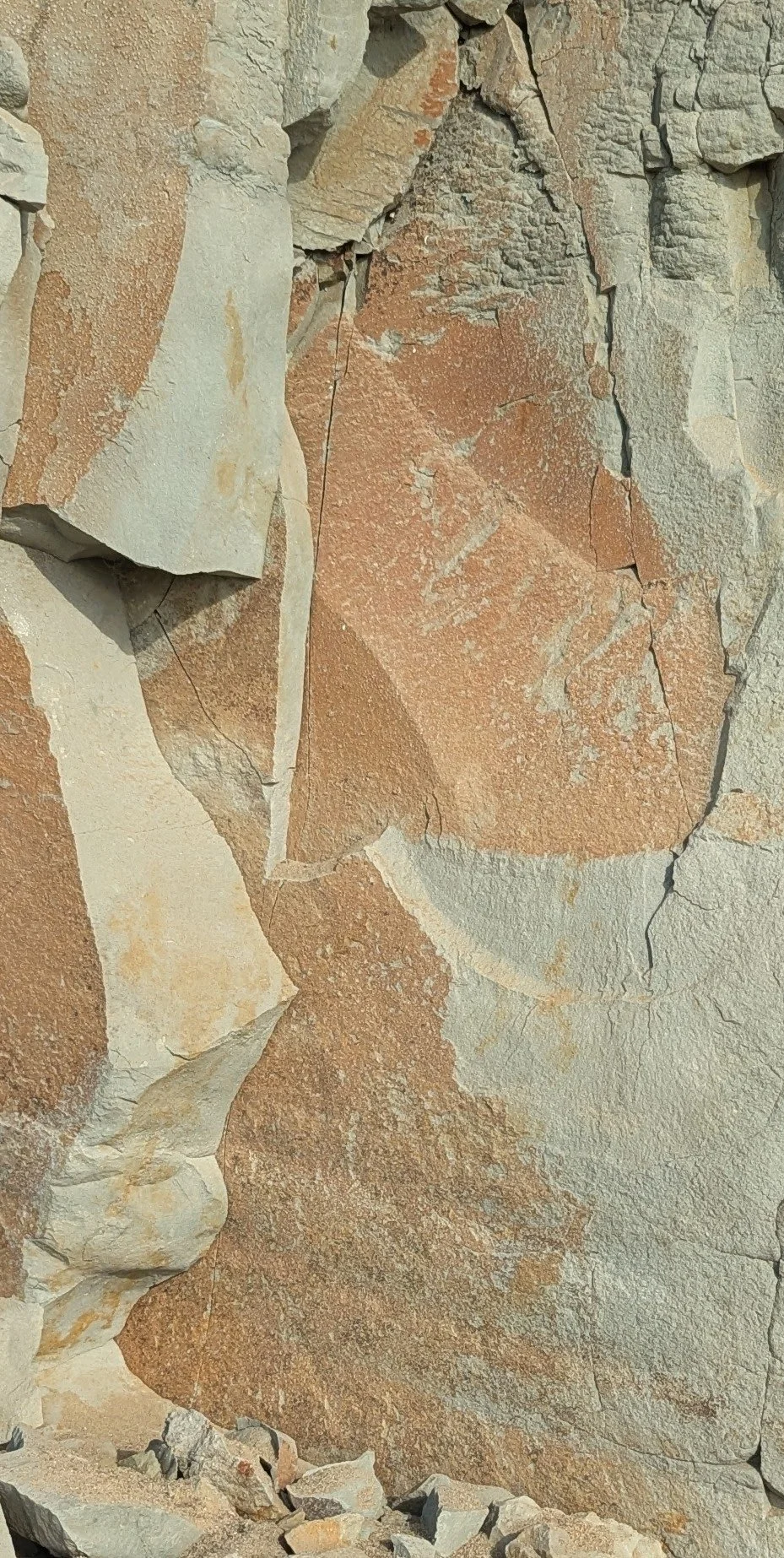 Close-up of a weathered stone wall with various cracks and layers of reddish-brown and beige rocks.