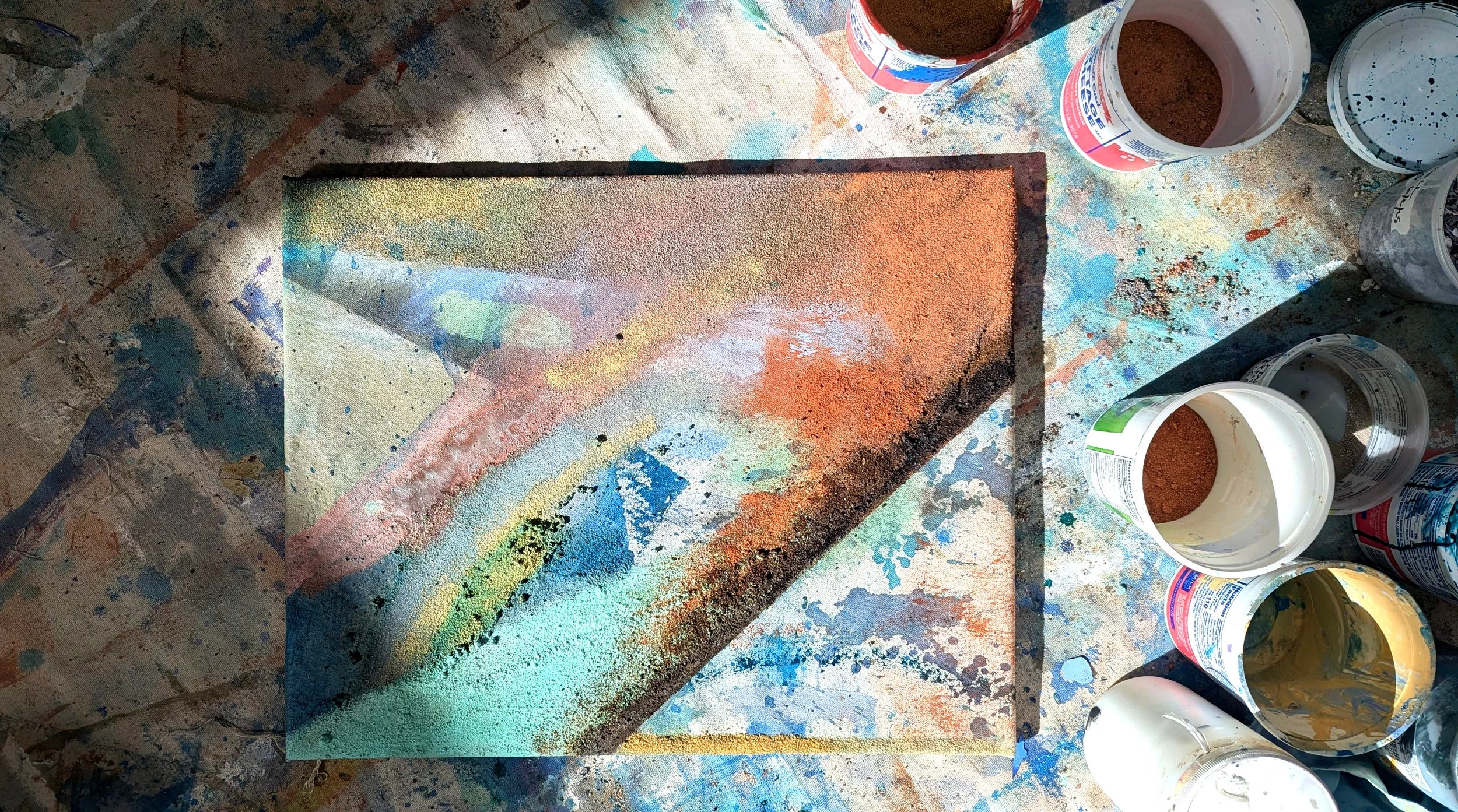 A colorful abstract artwork created with spray paint and mixed media, surrounded by open paint cans on a splattered table.