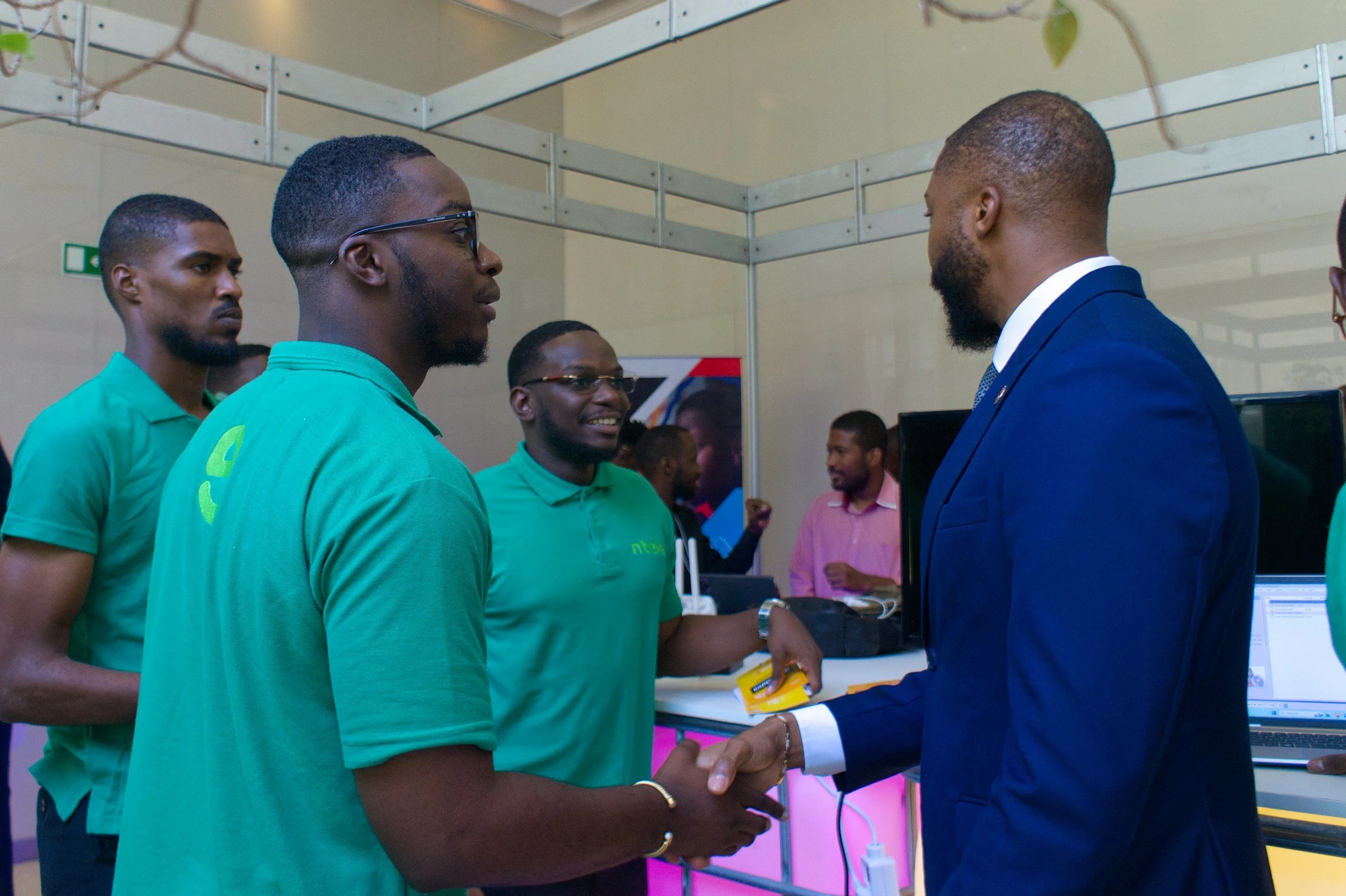 Man in a blue suit shaking hands with a man in a green shirt at a technology or business event.