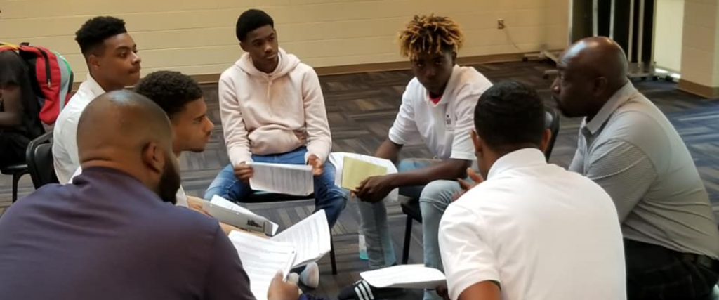 Group of seven people sitting in a circle and having a discussion or meeting.