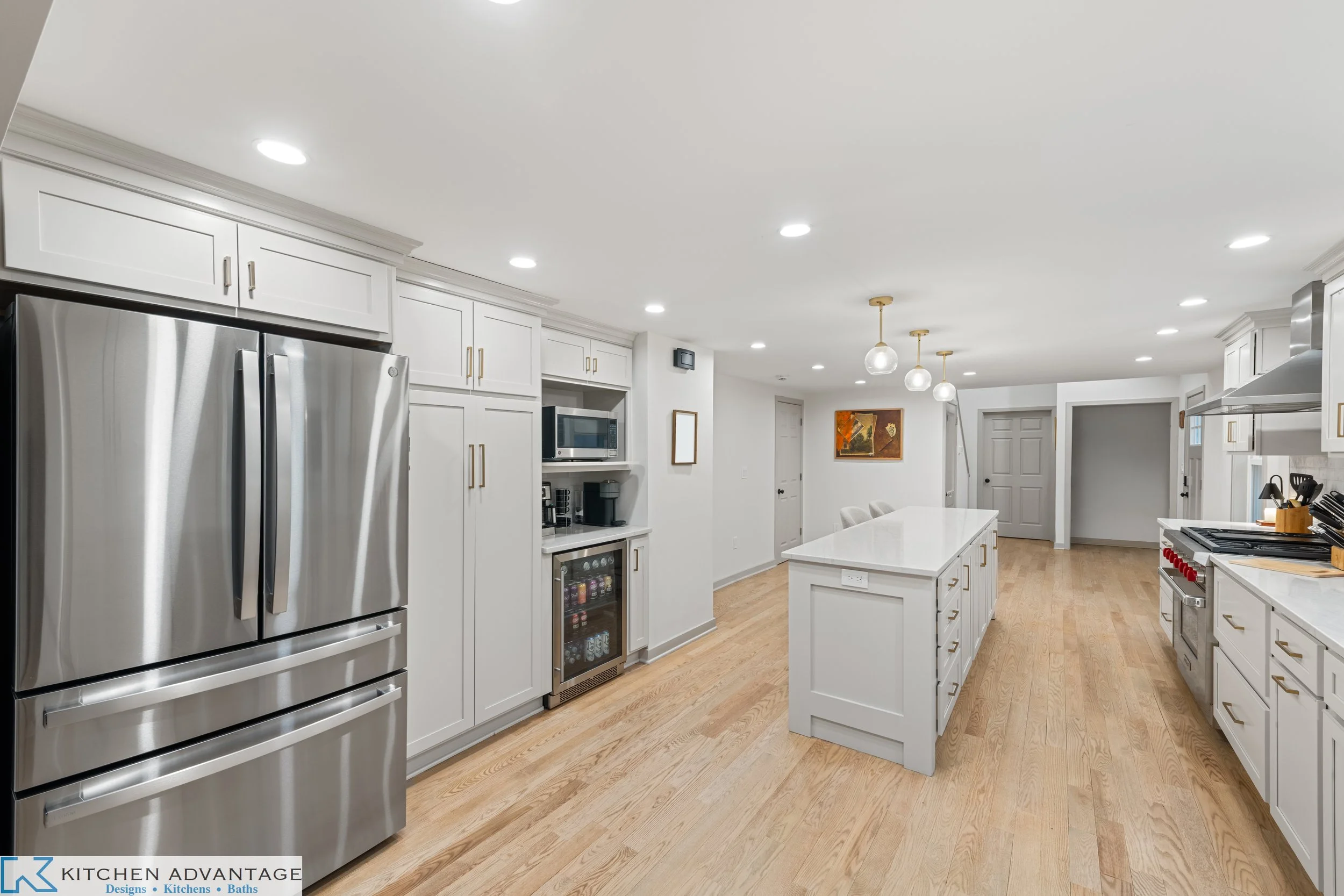 Kitchen with a long storage island, tall pantry cabinetry, refrigerator and coffee nook with a beverage refrigerator.