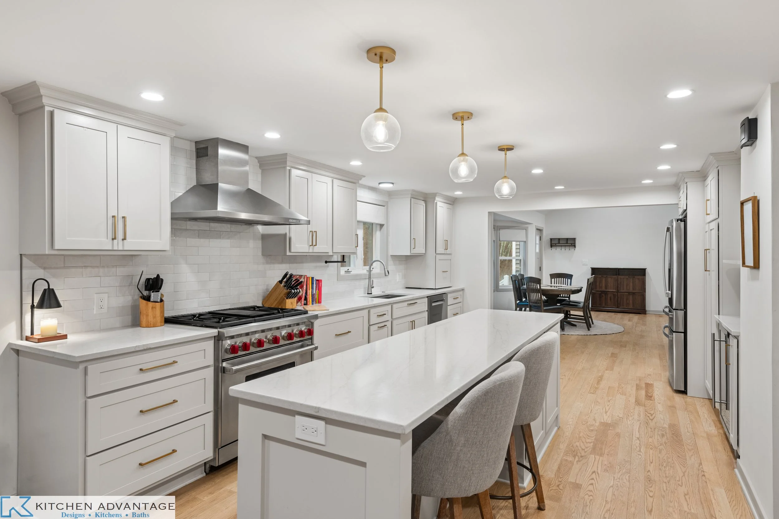 Woodbridge kitchen with soft white cabinetry, a long island with seating, globe pendant lights and a range with red knobs.