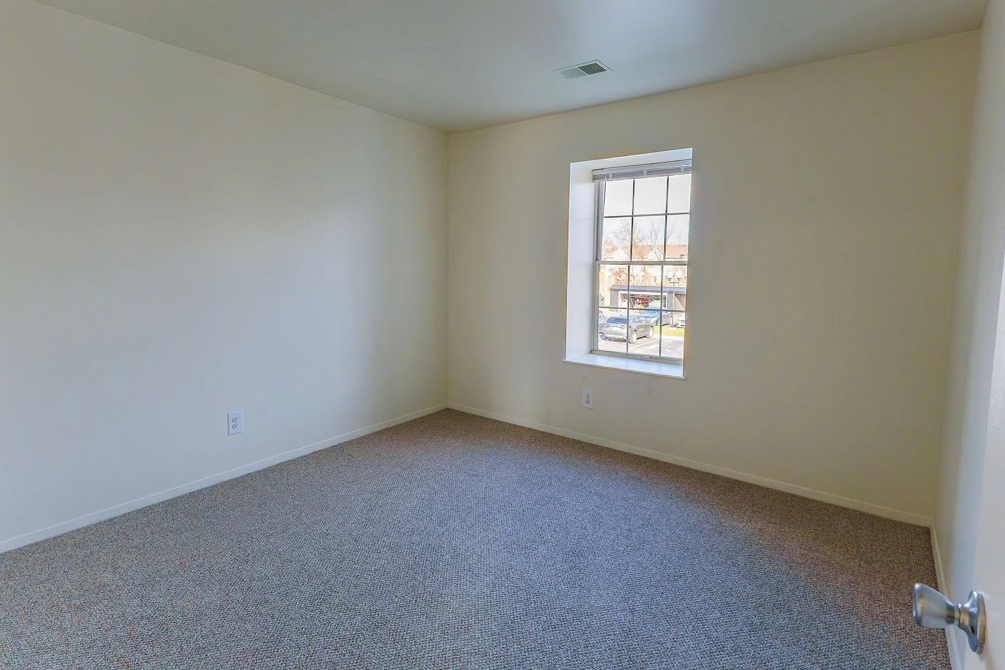 Empty room with beige carpet, white walls, a window with blinds, and a ceiling vent.