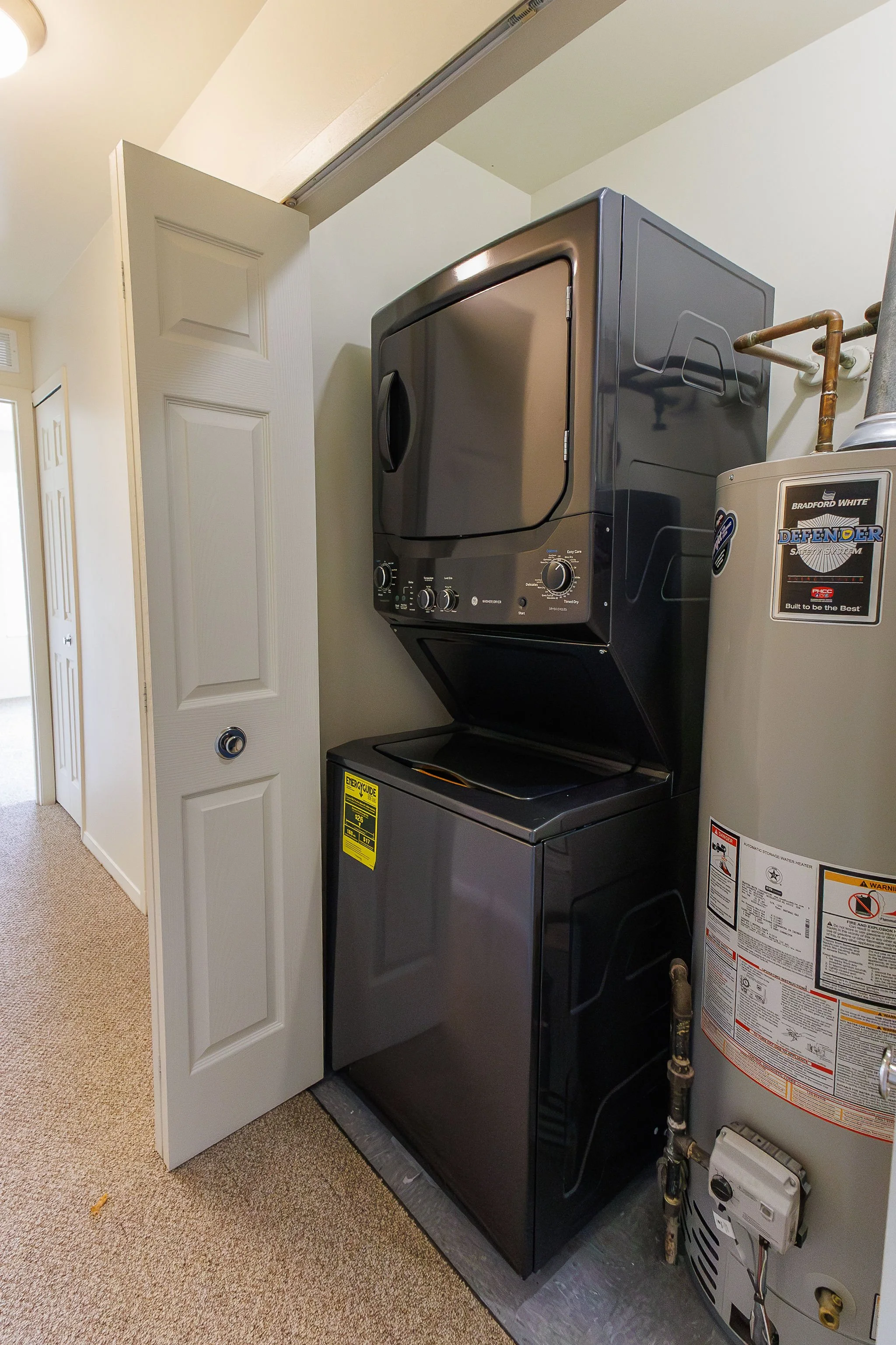 A stacked washer and dryer in a laundry room next to a water heater and a partially open closet door.