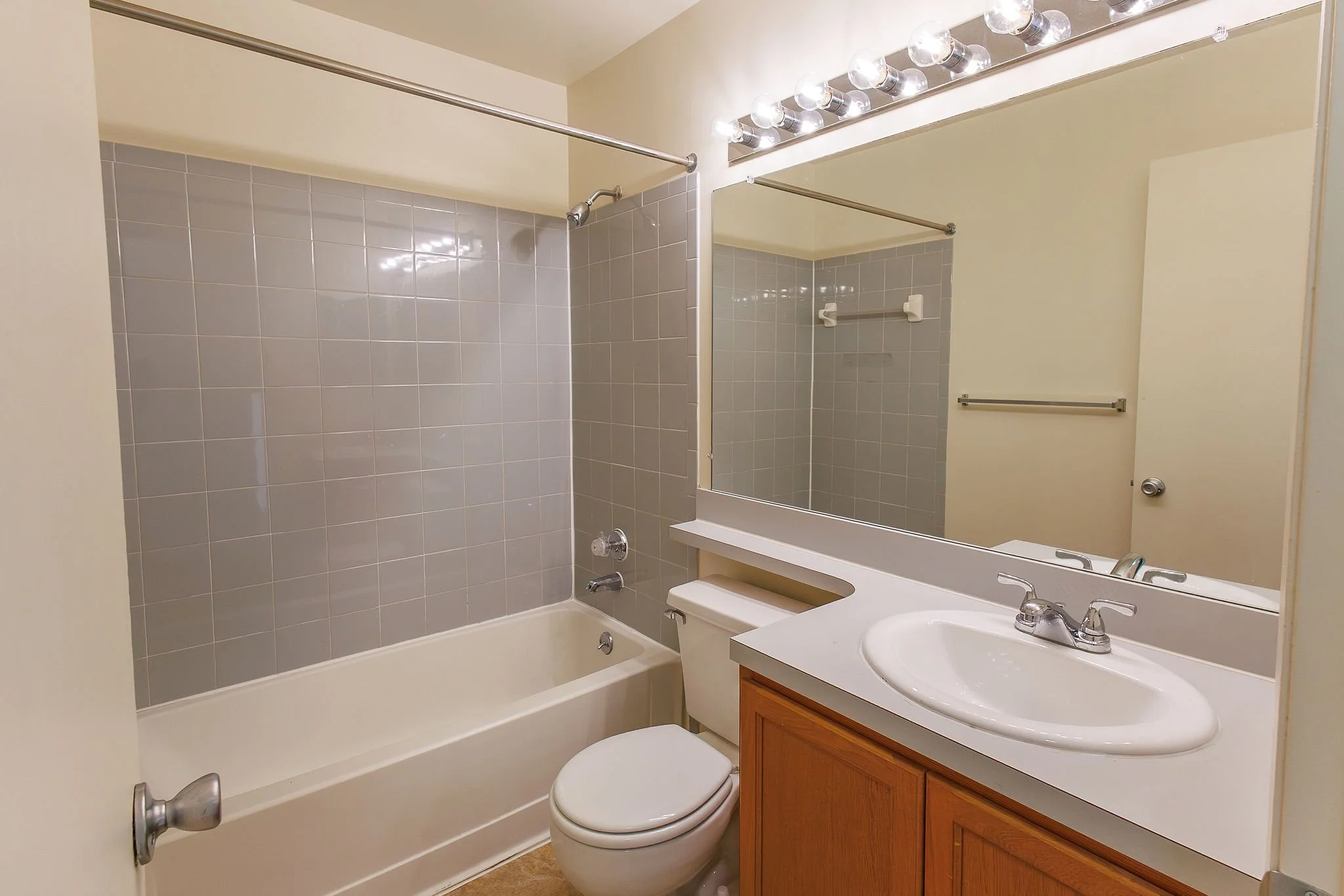 Bathroom with bathtub, toilet, sink, large mirror, gray tiled wall, and vanity cabinet.