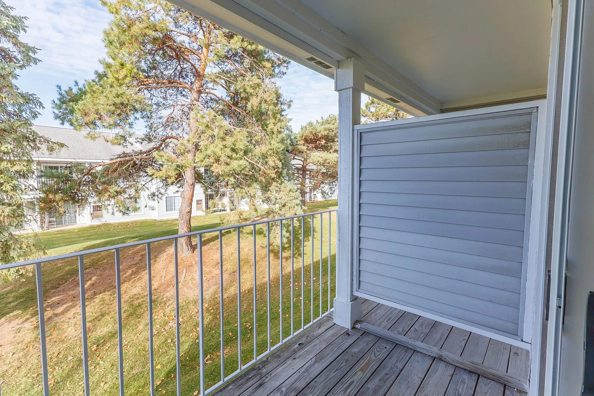 View from a balcony showing trees and a grassy area outside, with a neighboring building in the background.