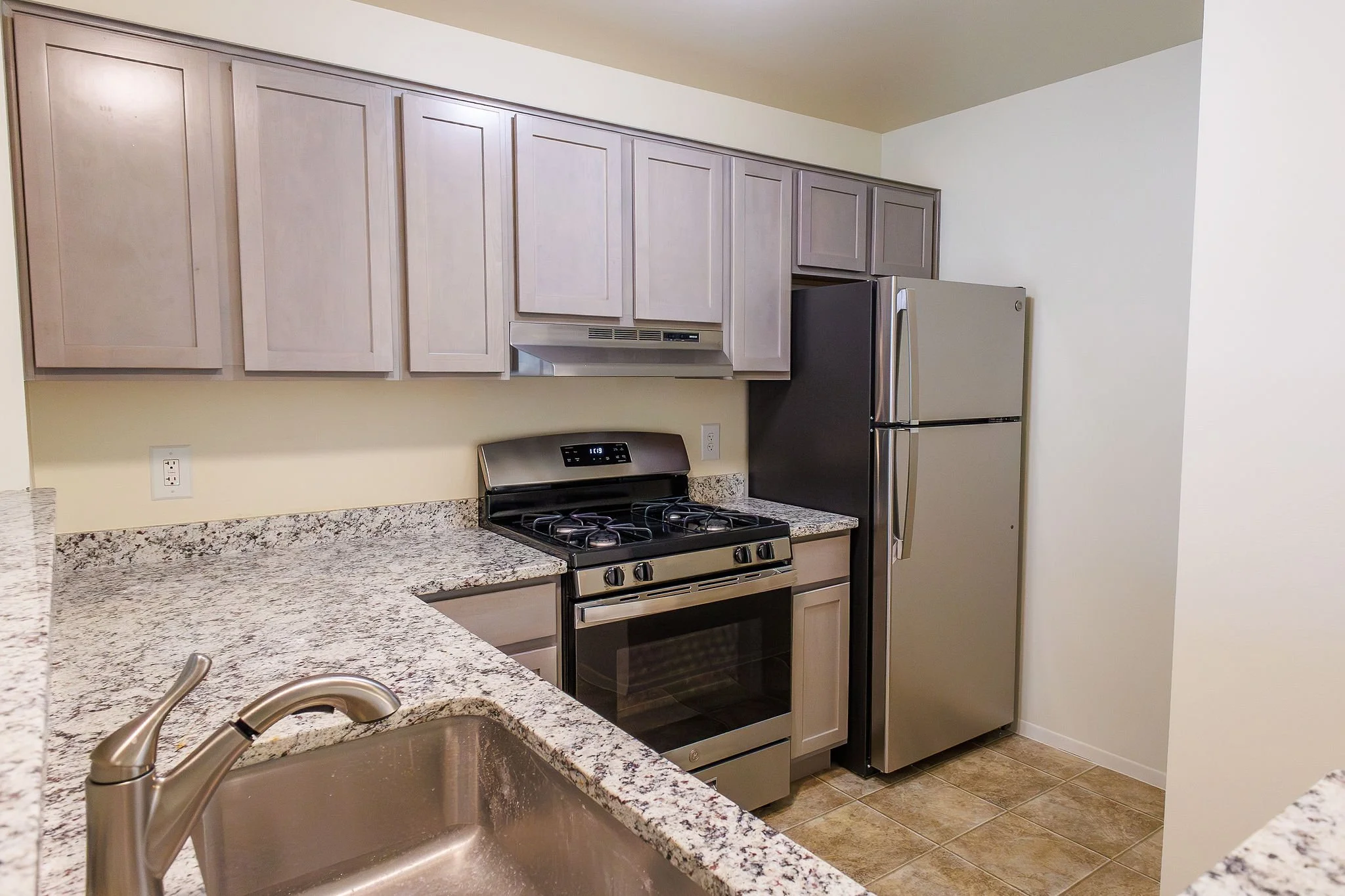 Kitchen with granite countertops, light wood cabinets, stainless steel refrigerator, stove, range hood, and a kitchen sink.