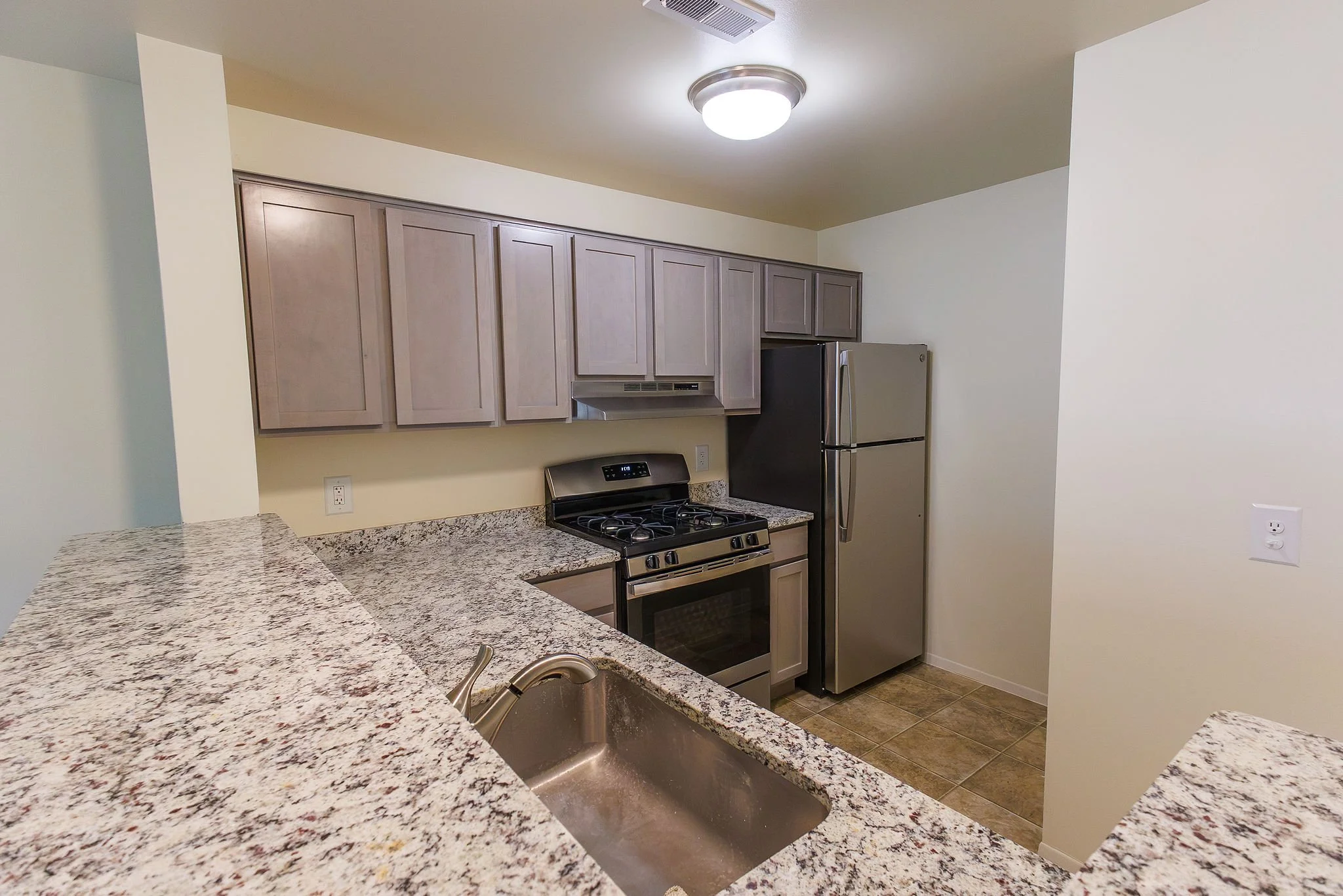 Modern kitchen with granite countertops, stainless steel refrigerator, black stove, beige cabinets, and a double sink.