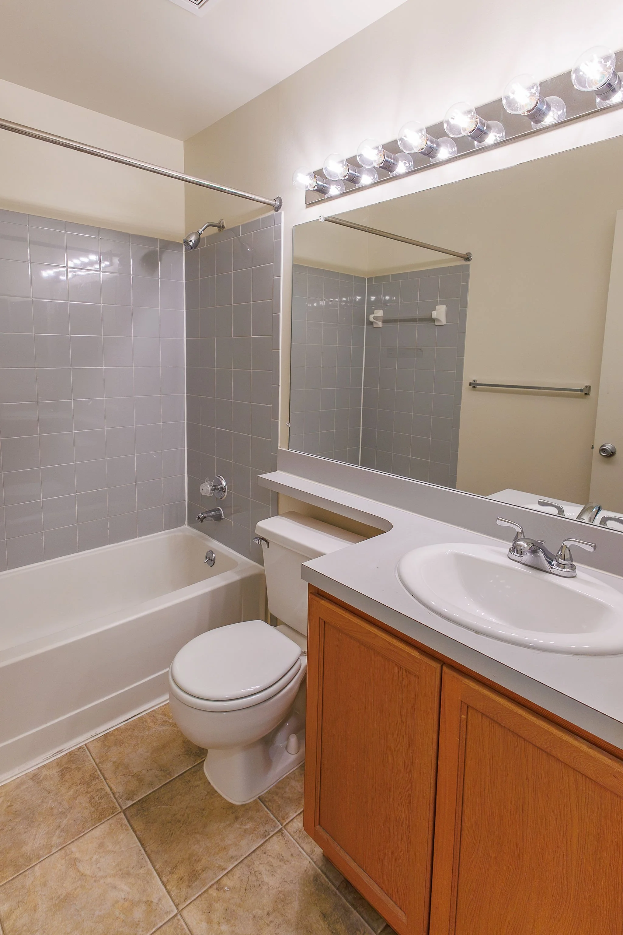 Bathroom with a bathtub, toilet, and wooden vanity with sink, large mirror, and vanity lights.