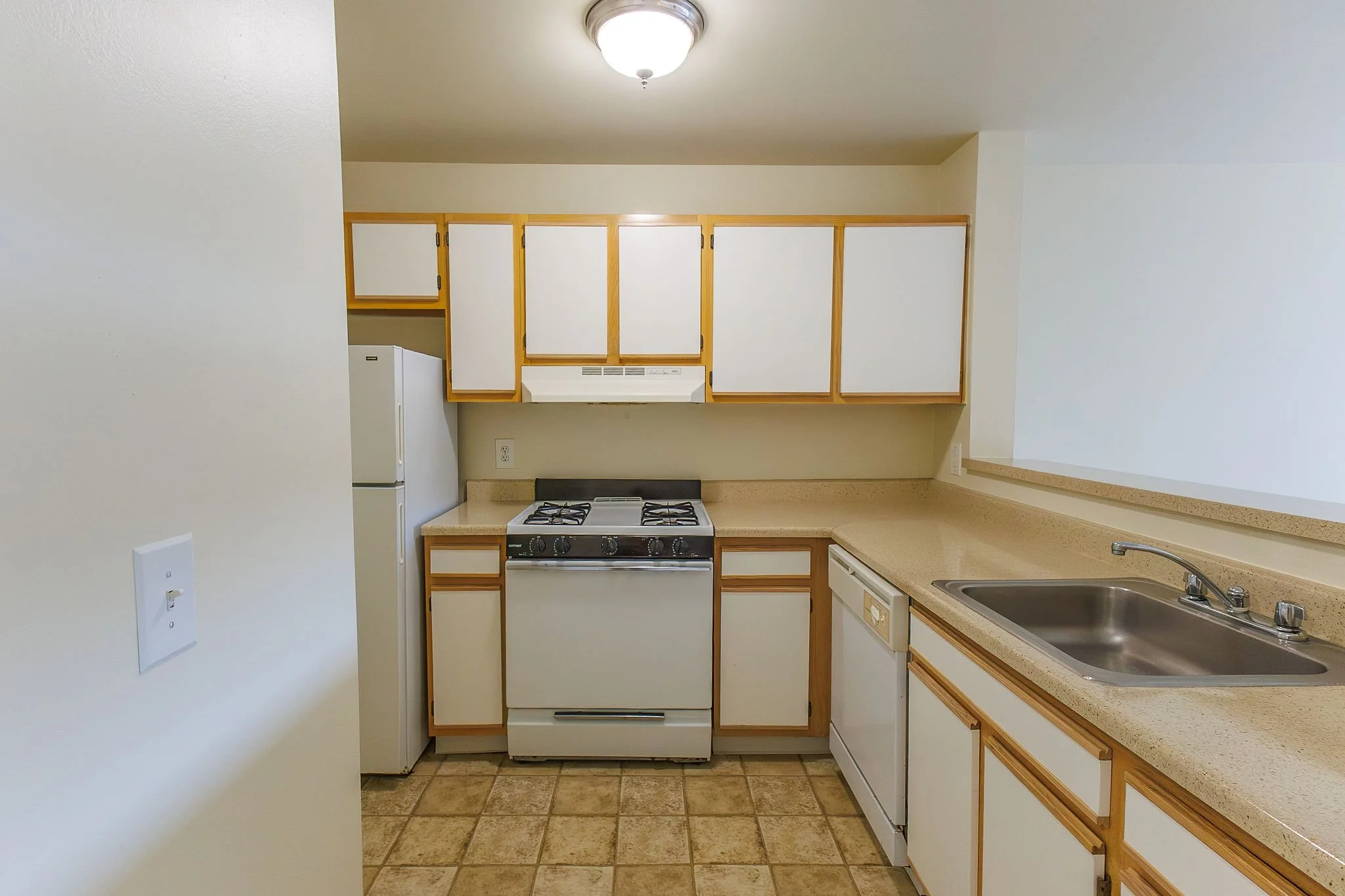 Kitchen with white cabinets, beige countertops, a stove, refrigerator, dishwasher, and a double sink.