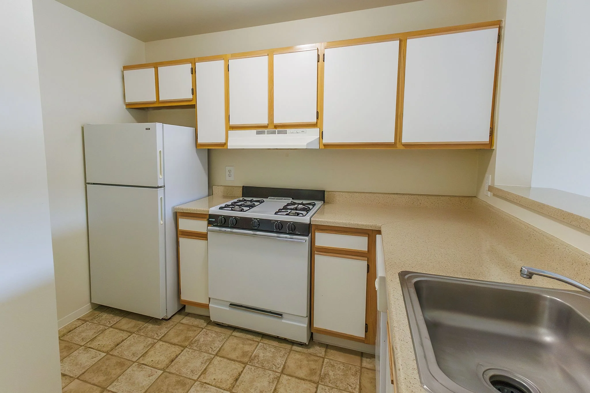 Kitchen with white appliances, beige countertops, wooden cabinets, a stove, and a stainless steel sink.