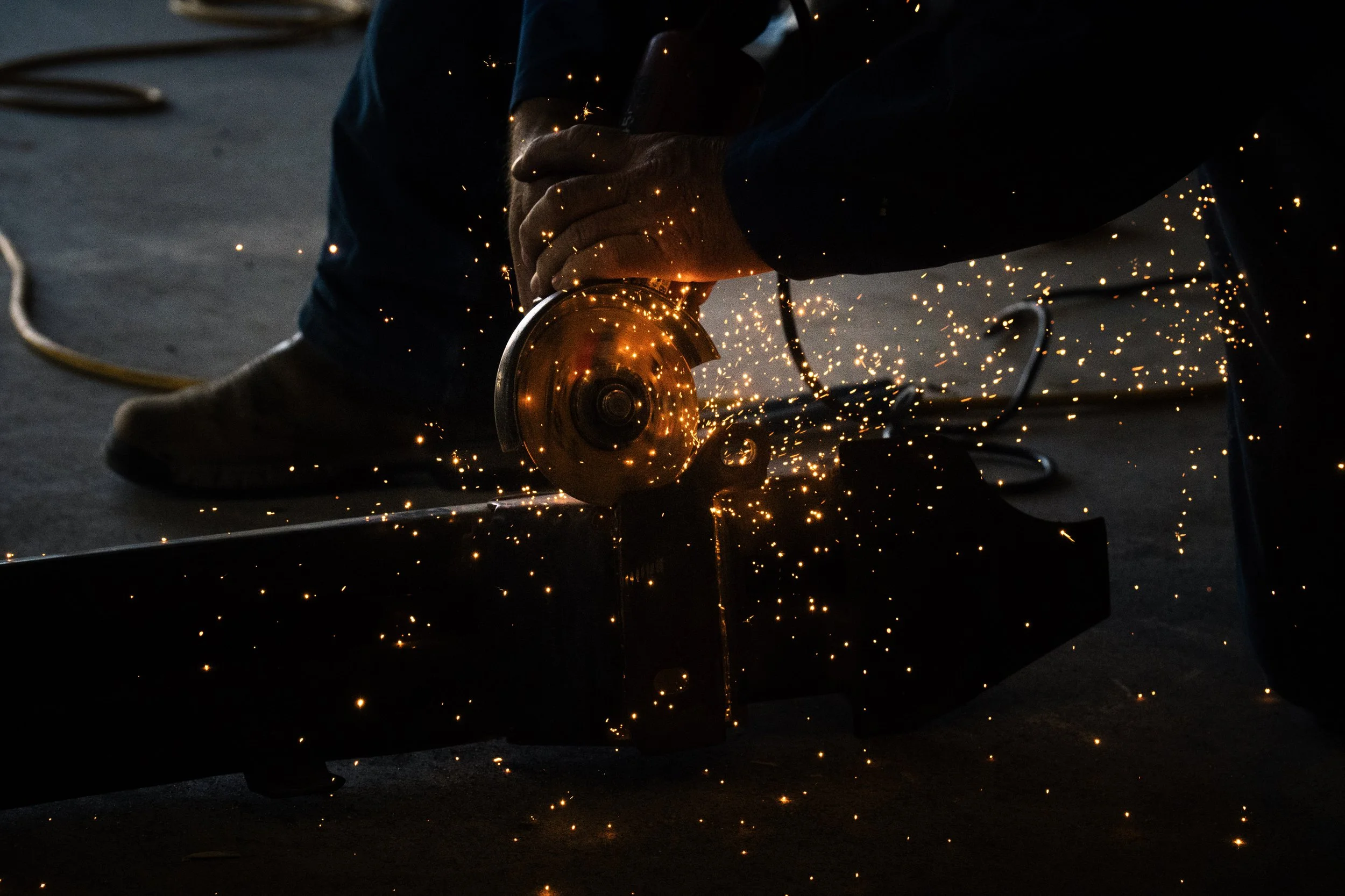 Person using an angle grinder, cutting metal and producing sparks during a welding or metalworking process.