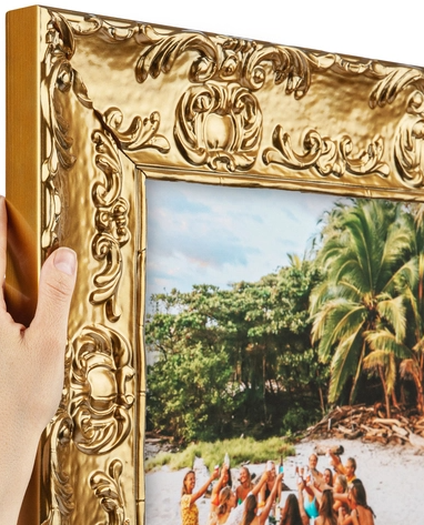 Close-up of a corner of an ornate gold picture frame holding a tropical landscape photo with palm trees and a group of people on the beach.