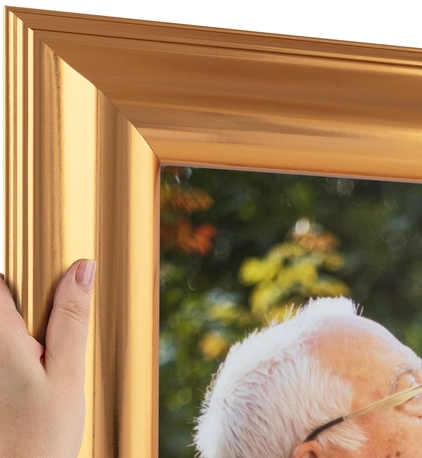 A person holding a wooden picture frame near a window, with a blurred outdoor scene visible in the background.