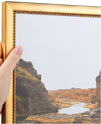 A hand holding a picture frame with an outdoor landscape scene of rocky cliffs and a river.