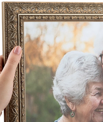 Close-up of an elderly woman smiling, her face partially visible, reflected in a decorative mirror held by a hand.