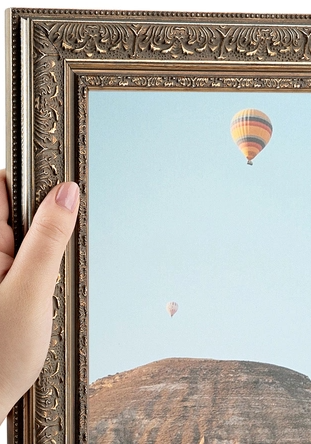 A person holding a decorative picture frame with a view of hot air balloons in the sky