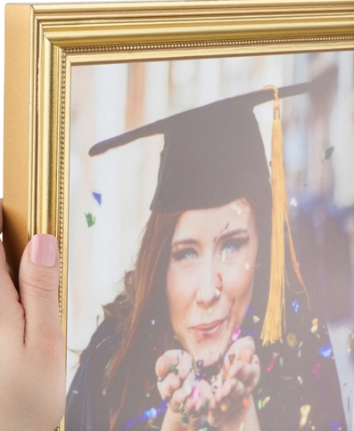 A framed graduation photo of a woman wearing a graduation cap, holding a handful of confetti and smiling.