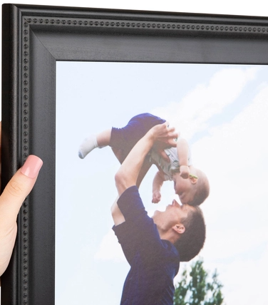A person holding a baby up in the air outside near a frame or mirror, with a blue sky and clouds in the background.