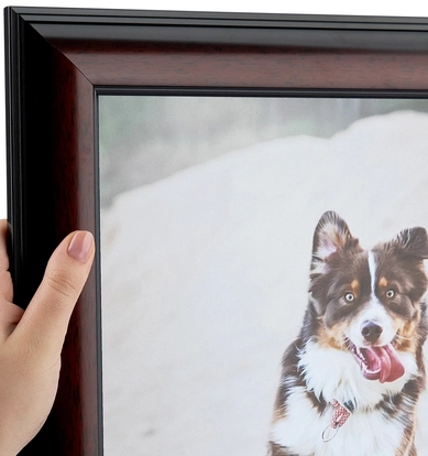 A person holding a framed photo of a dog with a snowy background.