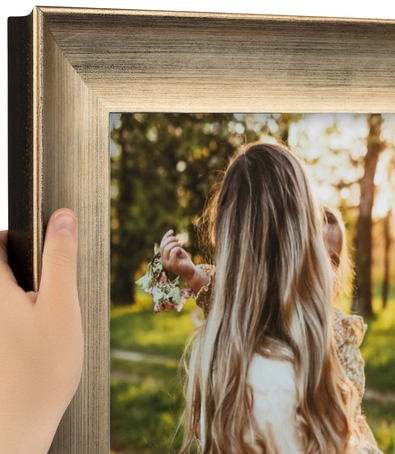 A person holding a framed photo of two young girls, one with long blonde hair, outdoors during sunset.