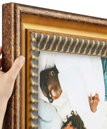 A person holding a framed photograph of a smiling man and woman lying together, with the man wearing sunglasses and a white shirt.