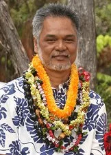 Man wearing floral shirt and multiple flower leis outdoors.