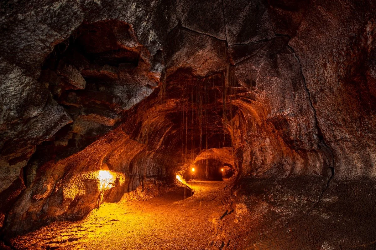 Inside view of a tunnel or mine with rough, reddish-brown rock walls illuminated by warm, orange lights.